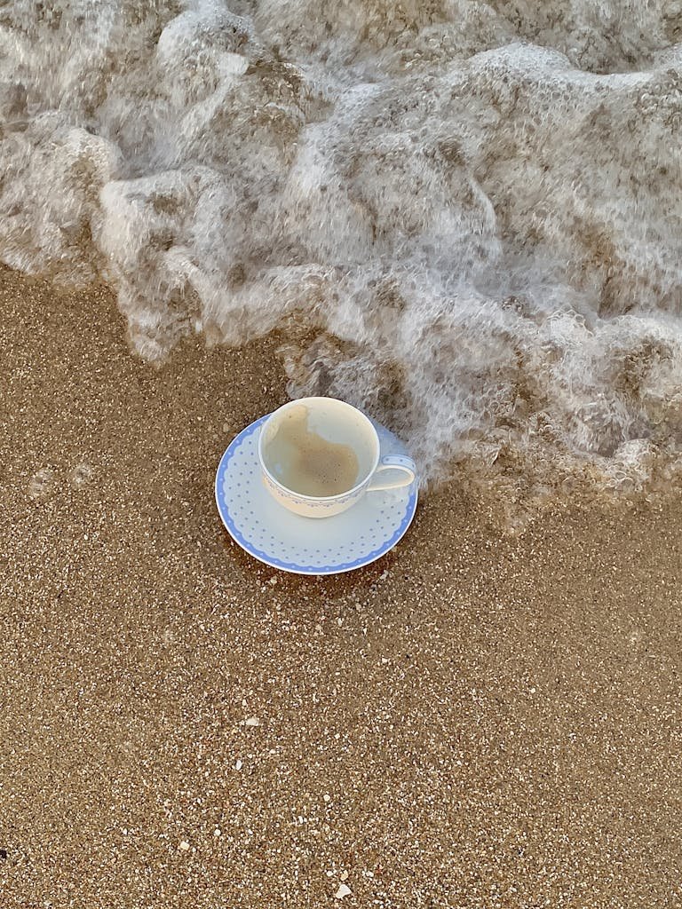 A EMPTY coffee cup with saucer on the sandy beach as waves approach, capturing a serene coastal moment.